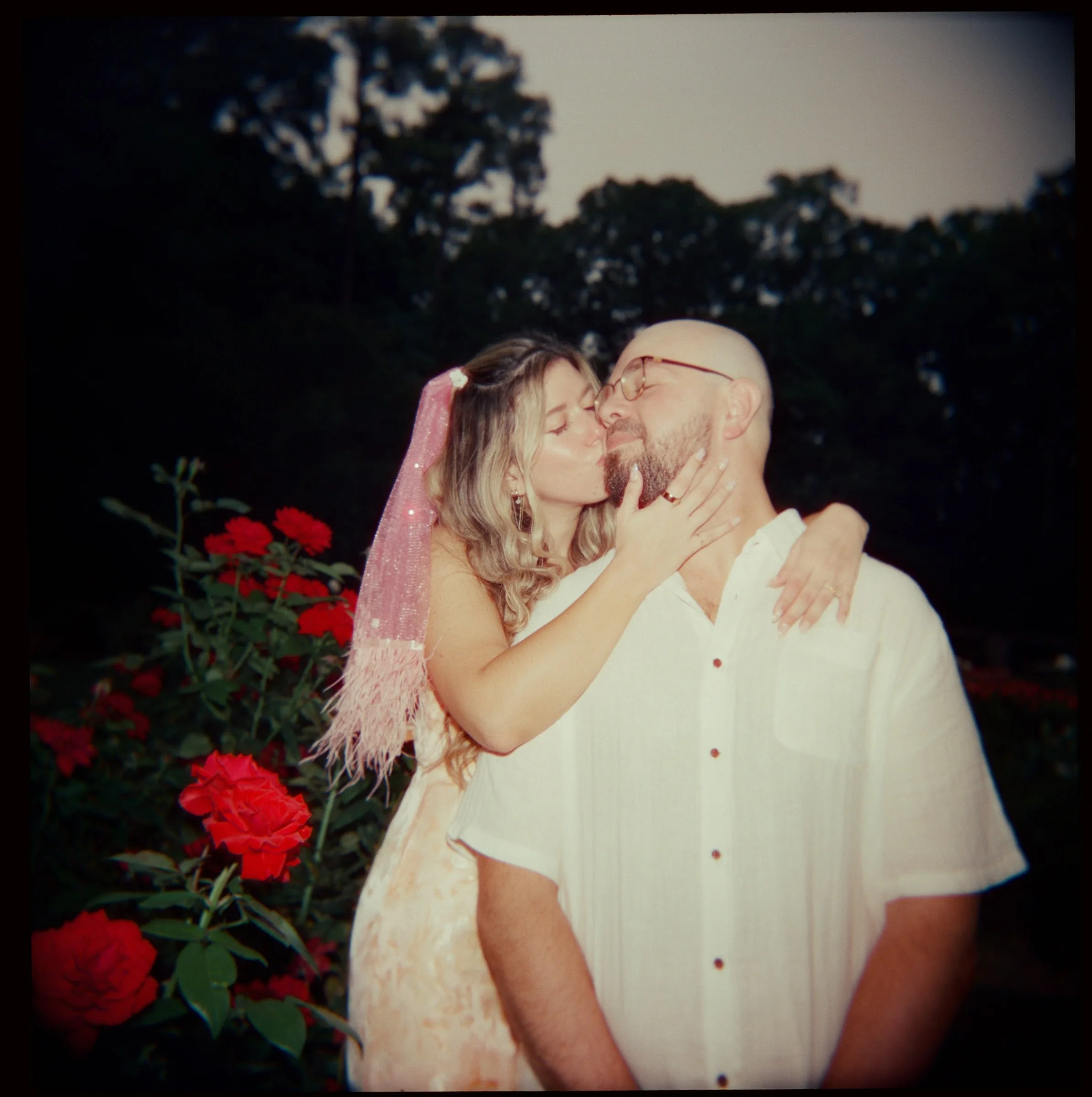 Nicole kissing Ian on the cheek at dusk beside red roses