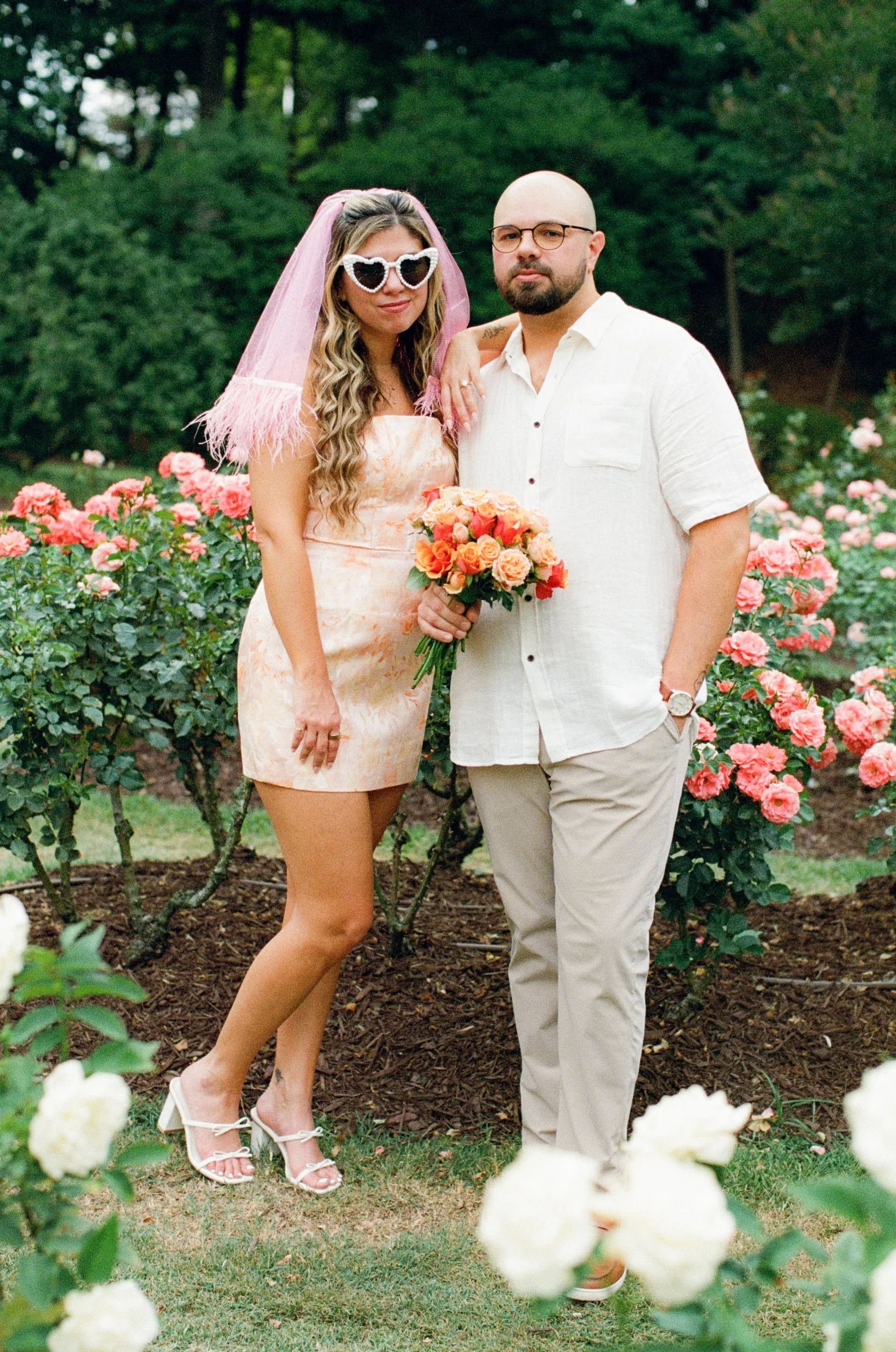 Nicole in heart-shaped sunglasses holding a bouquet, standing beside Ian